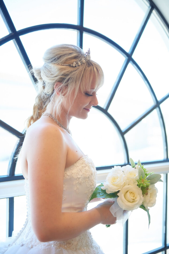 Beautiful bride standing by a glass window holding a wedding bouquet